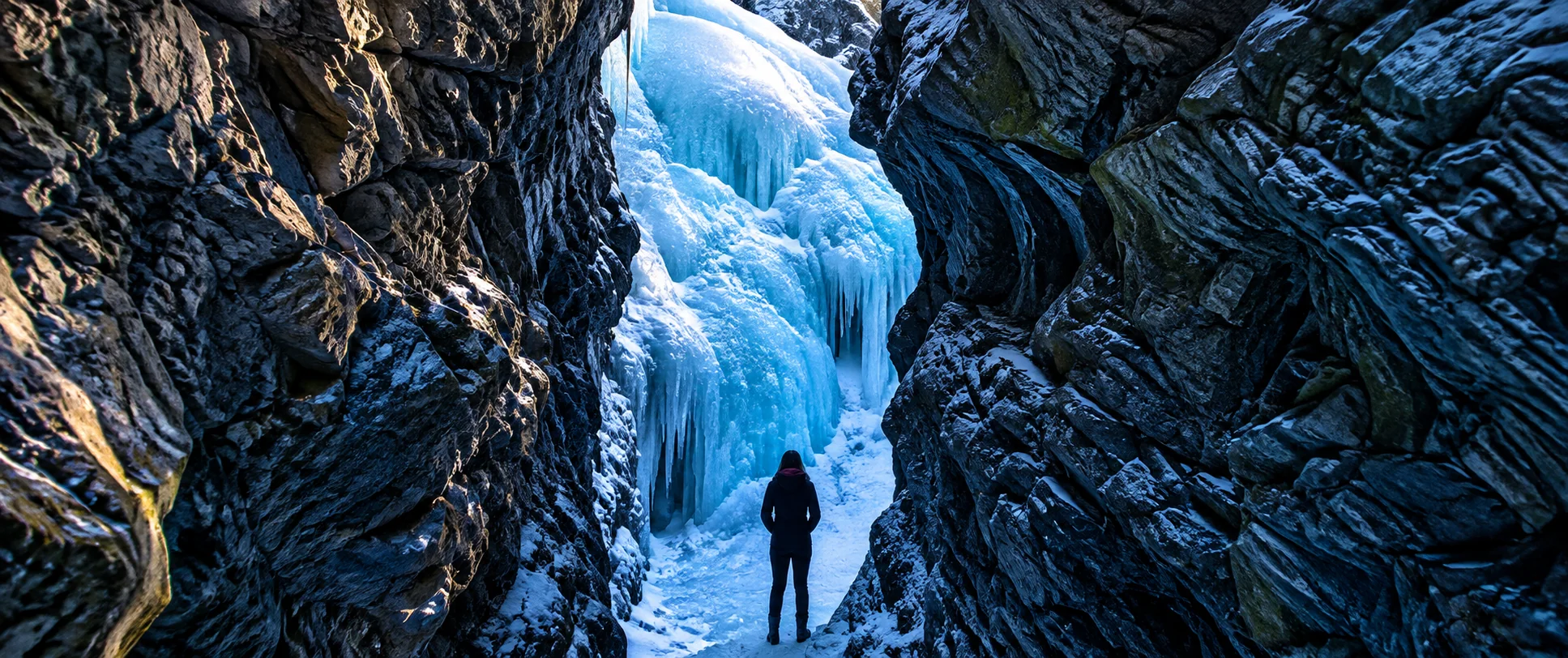 A lone visitor looks toward towering blue ice at a frozen waterfall.